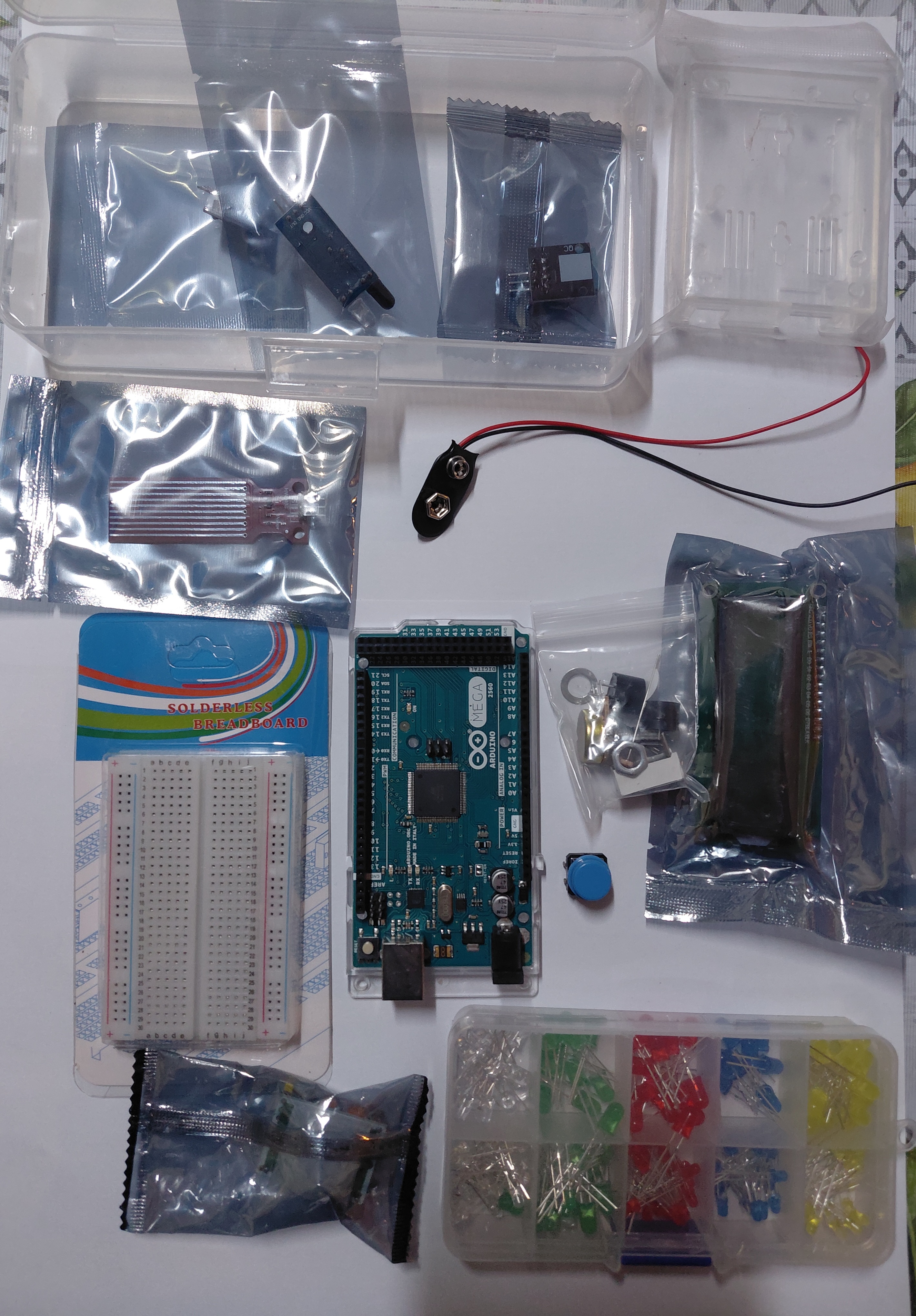 Arduino Mega 2560 kit laid out on a table showing the board, breadboard, LEDs, rain sensor, I2C module, LCD display, button and 9V battery connector