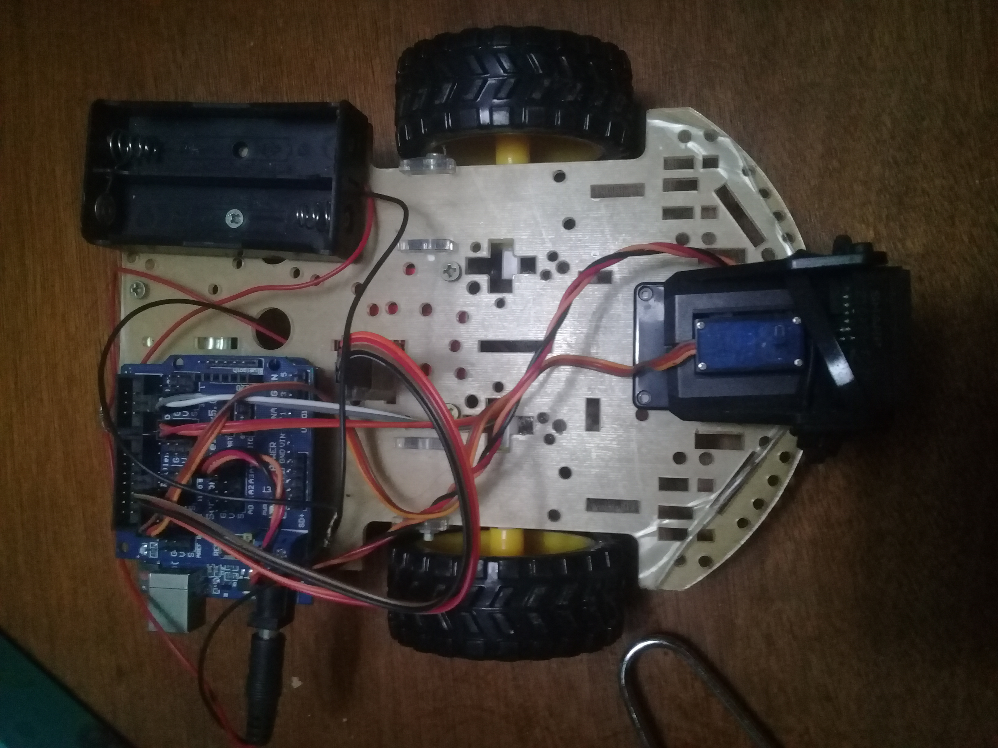Top-down view of a student-built 4WD Arduino robot car showing Arduino board, motor driver, battery pack and wiring on a white plastic chassis