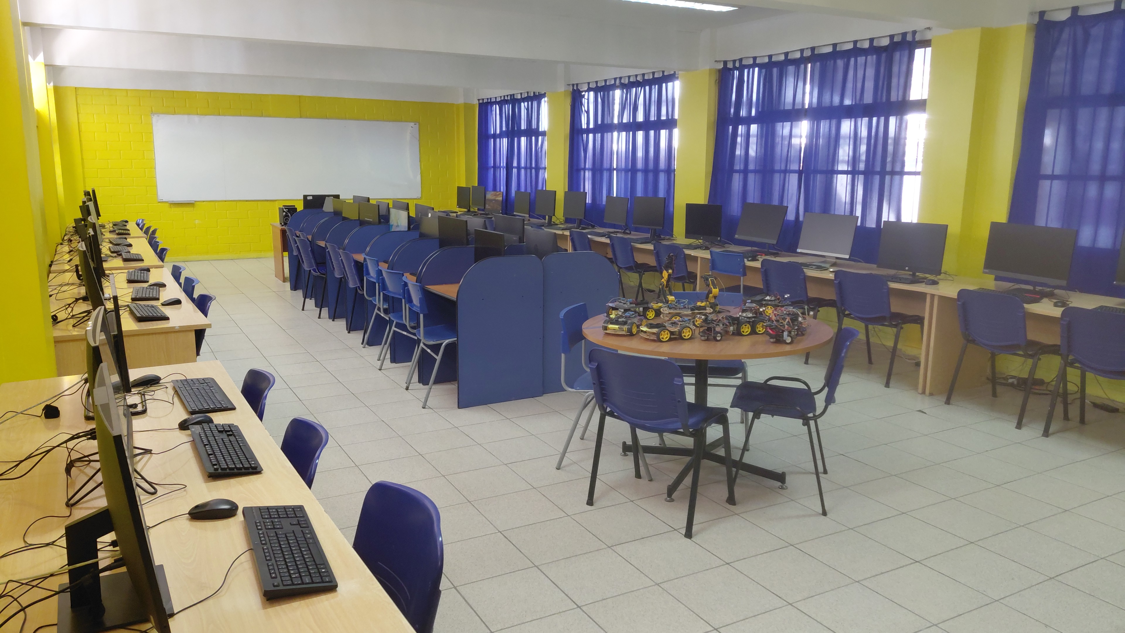 The school robotics lab with computers along the walls and robot cars on a central round table, room empty before class
