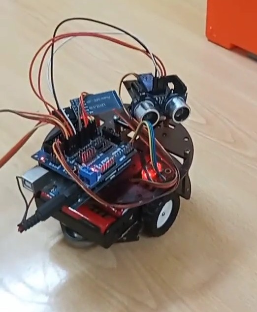 Close-up of the robot car's wiring: Arduino, motor driver shield and HC-05 Bluetooth module stacked on top of the chassis, red LEDs lit