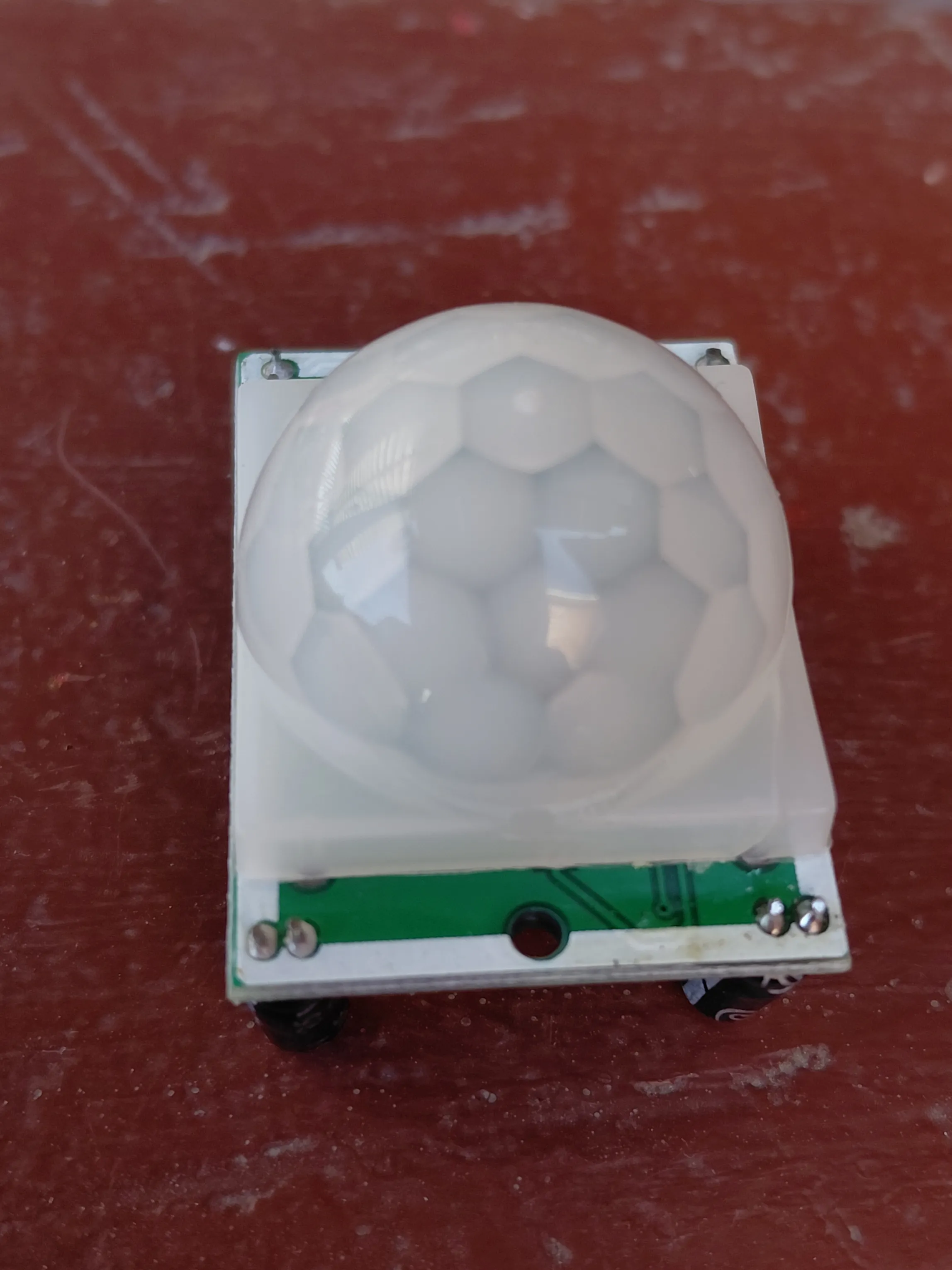 HC-SR501 PIR motion sensor module seen from above, showing the white segmented Fresnel lens dome mounted on the green circuit board