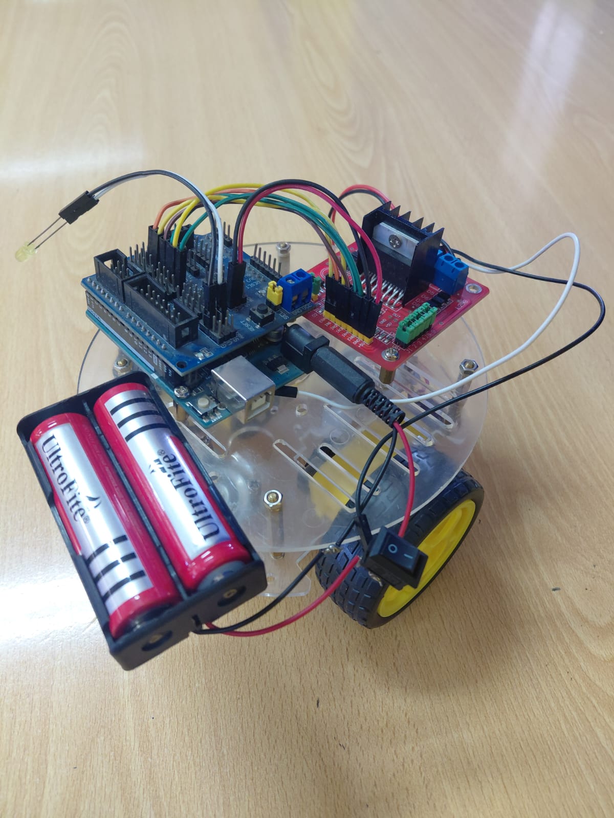 Side view of the same robot showing two Ultrafire 18650 Li-ion cells in a holder, red motor driver board, Arduino Mega, and clear acrylic chassis base