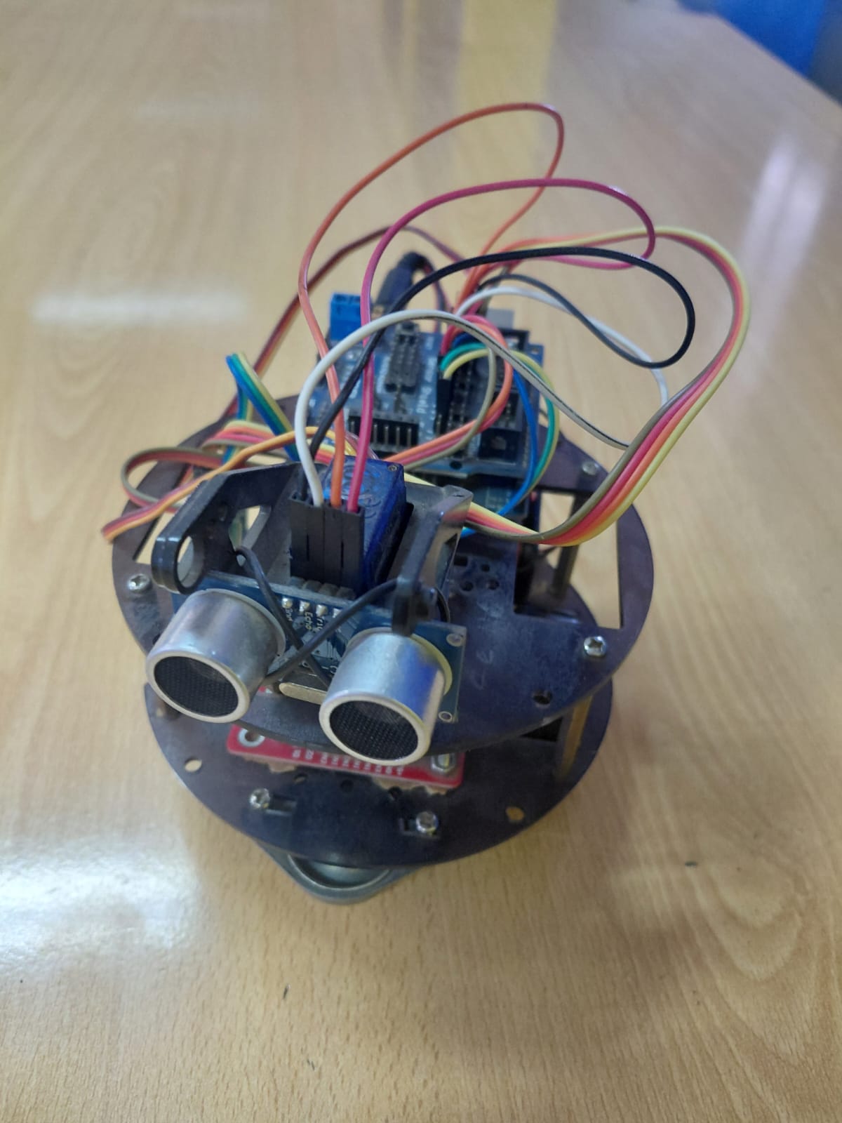 Front view of round black robot chassis with two HC-SR04 ultrasonic sensors side by side, heavy rainbow-colored wiring, and Arduino Nano visible at the top