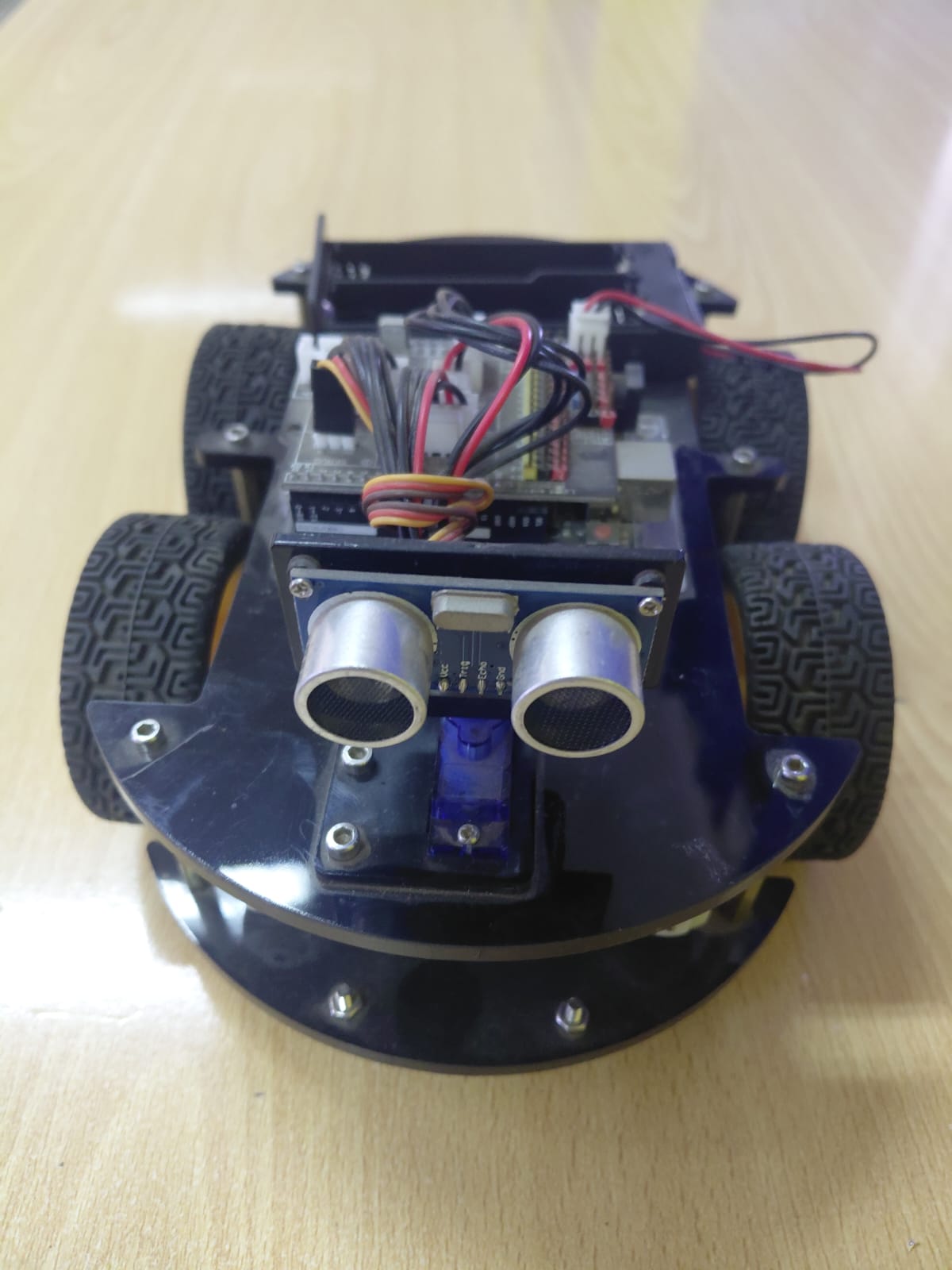 Front close-up of 4WD robot with a single HC-SR04 ultrasonic sensor mounted on a small servo motor, battery holder visible at the back, blue acrylic chassis