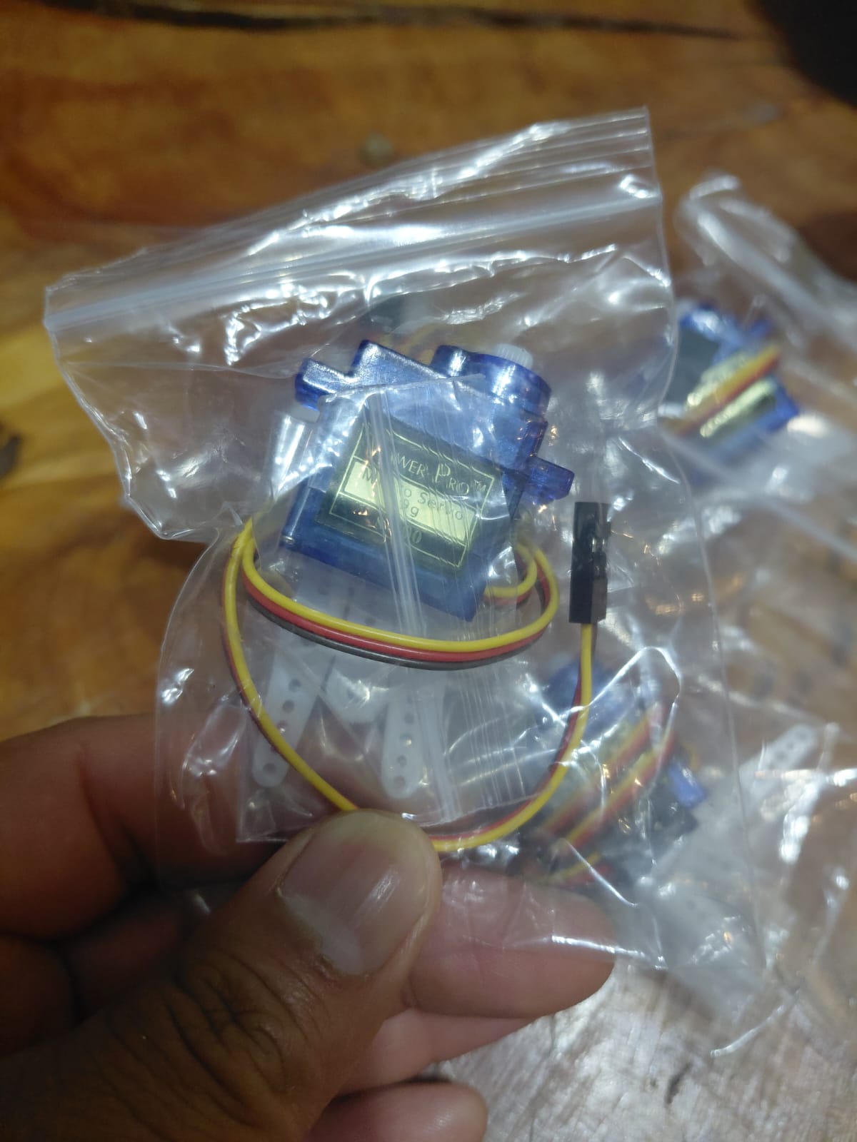 SG90 servo in its plastic bag showing the Tower Pro label with specifications printed on the sticker, with horn attachments and wiring visible